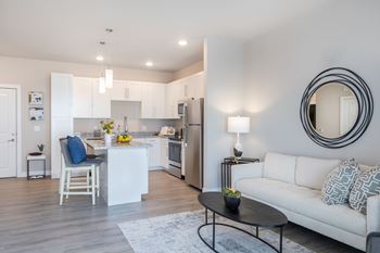 A modern kitchen with a white island and a white couch with a grey and white pillow.